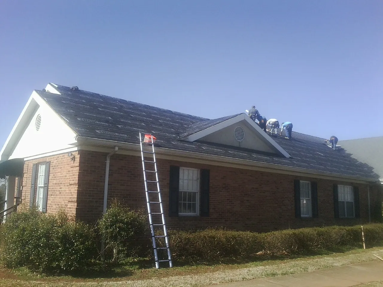 Crew tearing shingles off a brick ranch roof with a ladder set — Emergency Roof Repair work by our crew in Ashburn
